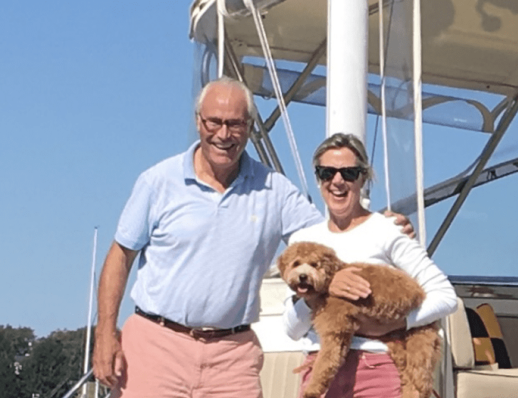 Candace and Larry stand on boat, holding a dog