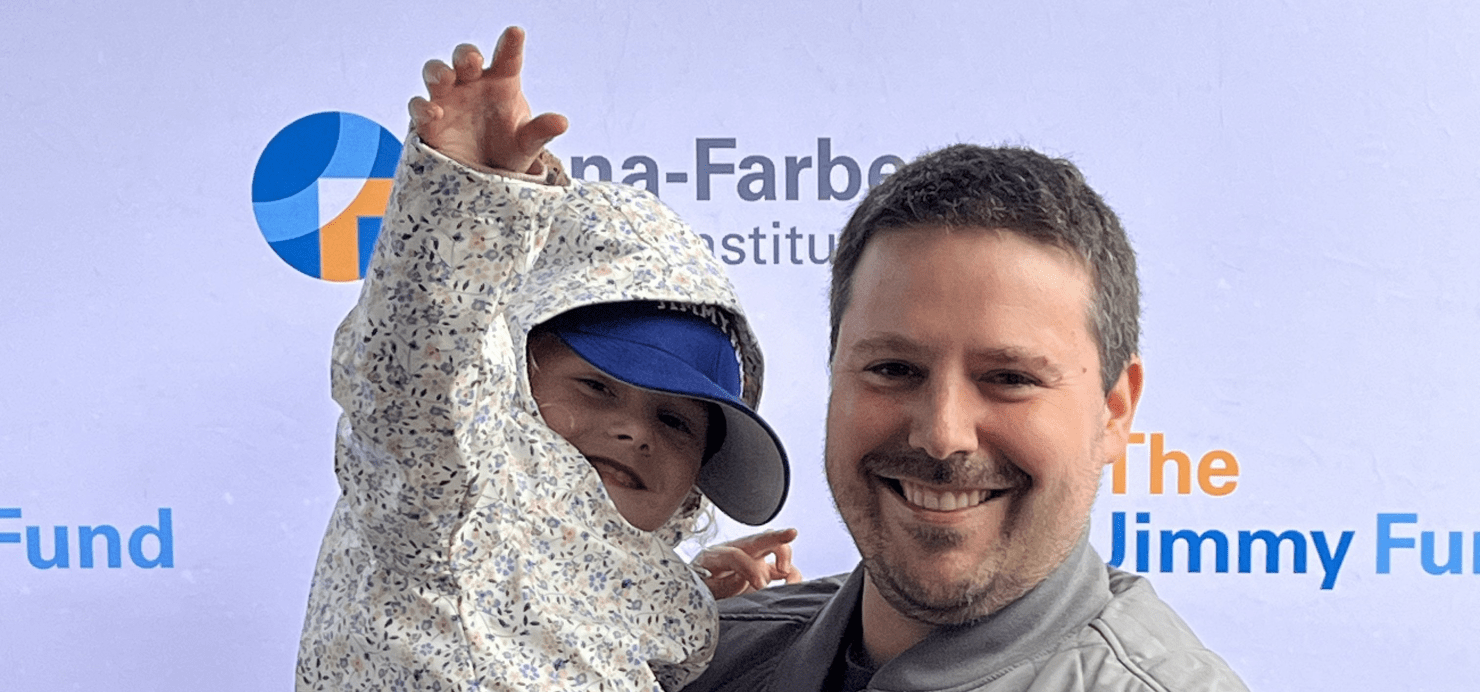 Dad holds child in front of Dana-Farber and the Jimmy Fund backdrop